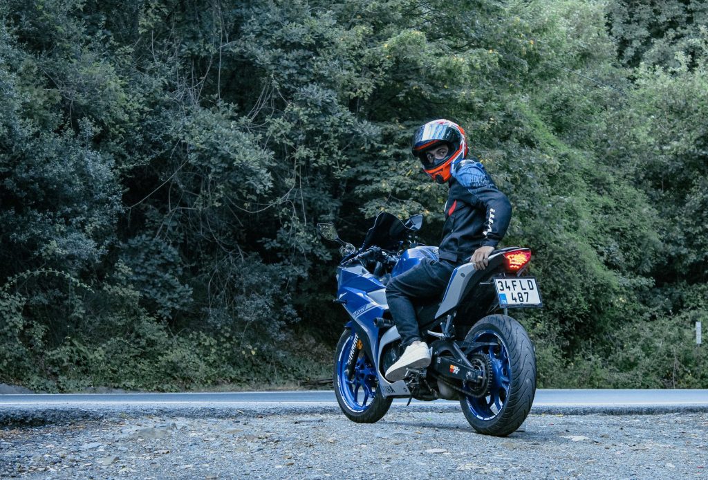 Motociclista usando capacete conduz uma motocicleta Yamaha azul por uma estrada cercada de vegetação.