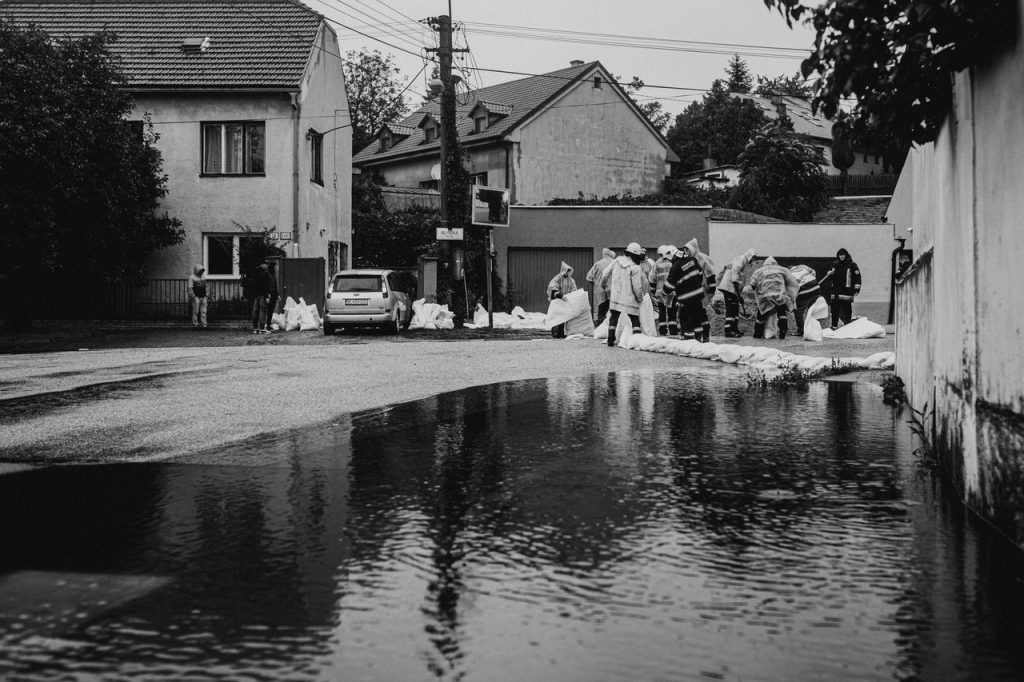 Voluntários usando capas de chuva colocam sacos de areia para conter alagamento em uma rua urbana.
