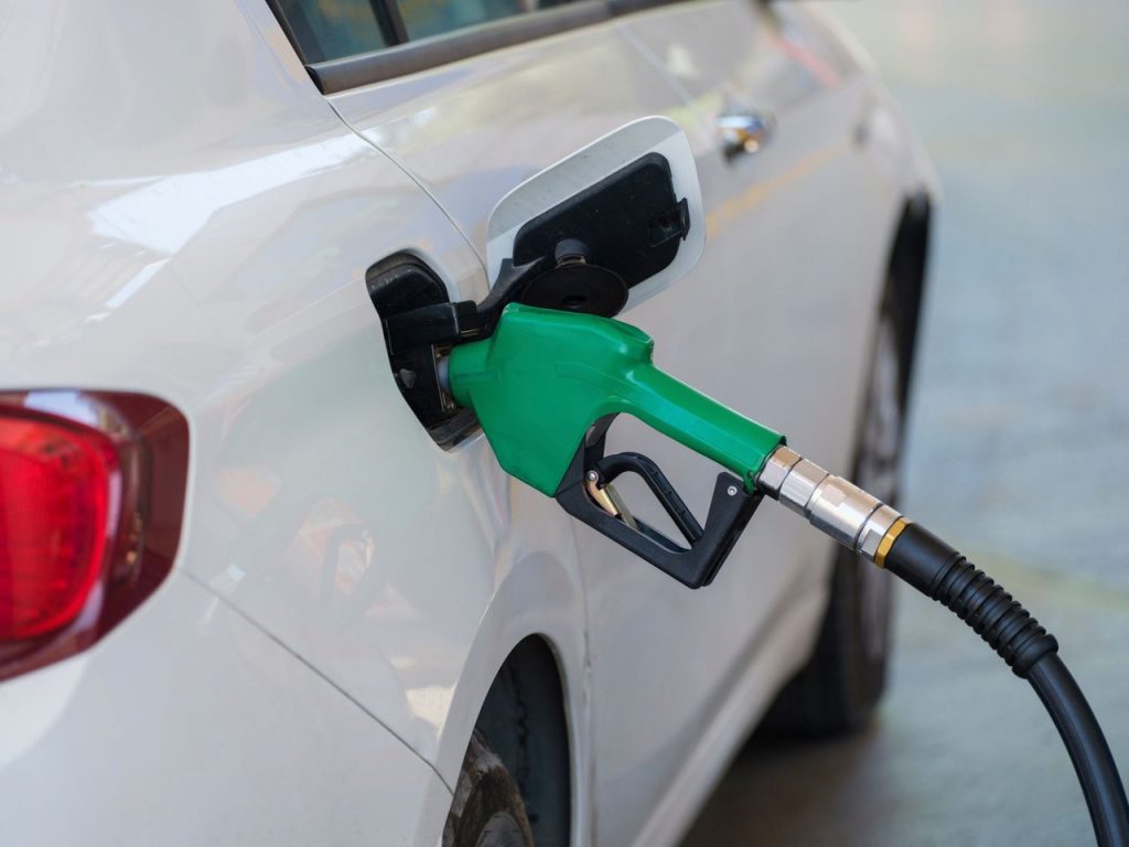 O que muda para quem abastece com gasolina, etanol ou GNV em outubro de 2026 Close de um bico verde abastecendo um carro branco em um posto de combustíveis.