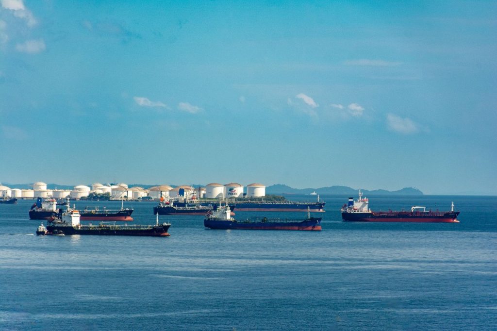 Diesel coloca segurança energética global no centro da nova decisão da IEA Navios cargueiros atracados junto a tanques de armazenamento de petróleo em uma área industrial costeira.