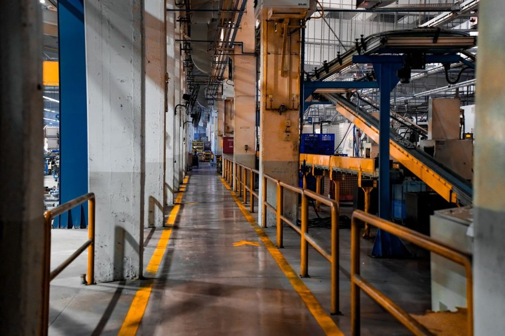 Interior amplo de uma fábrica moderna, com máquinas industriais e sistemas de esteiras em operação.